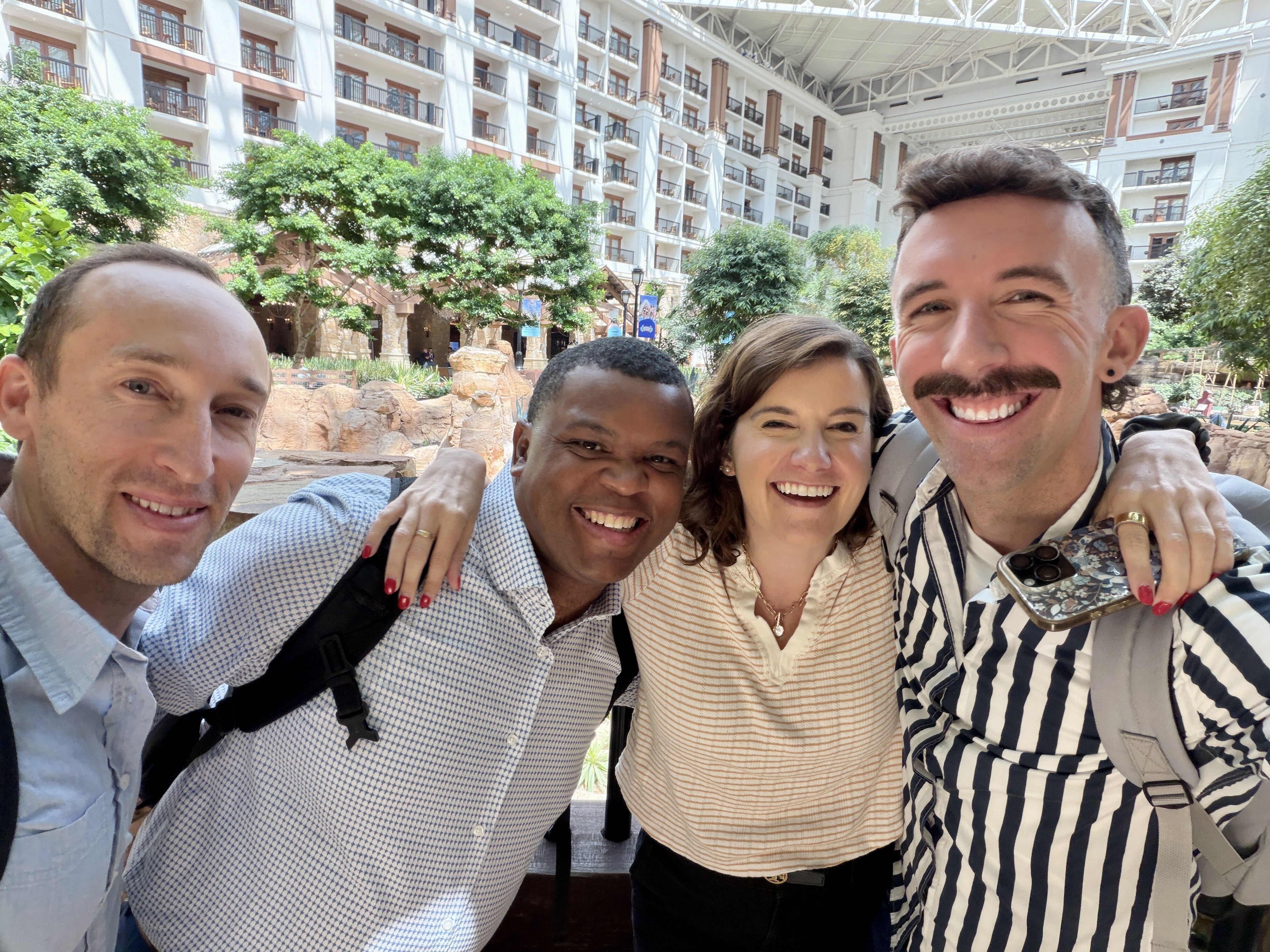 Four Alltus team members smiling together in a sunlit hotel atrium